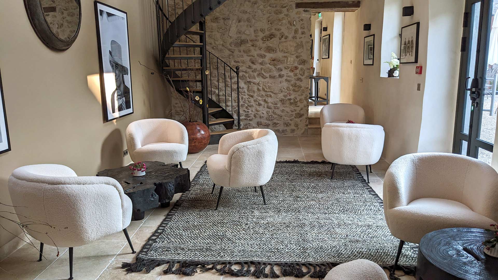 Salon élégant avec des fauteuils blancs arrondis, une table basse en bois sculpté, un tapis texturé et un escalier en colimaçon en métal, dans la pièce de séjour de la maison d'hôtes Val Trebbia